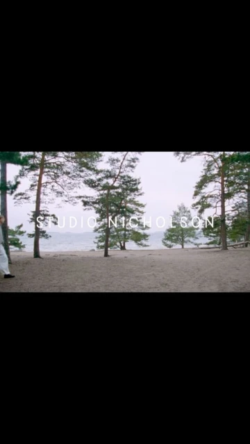 Scenic outdoor shot showcasing a sandy path lined with tall pine trees and a serene lake under a cloudy sky, featuring the Studio Nicholson logo.