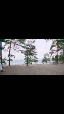 Scenic outdoor shot showcasing a sandy path lined with tall pine trees and a serene lake under a cloudy sky, featuring the Studio Nicholson logo.