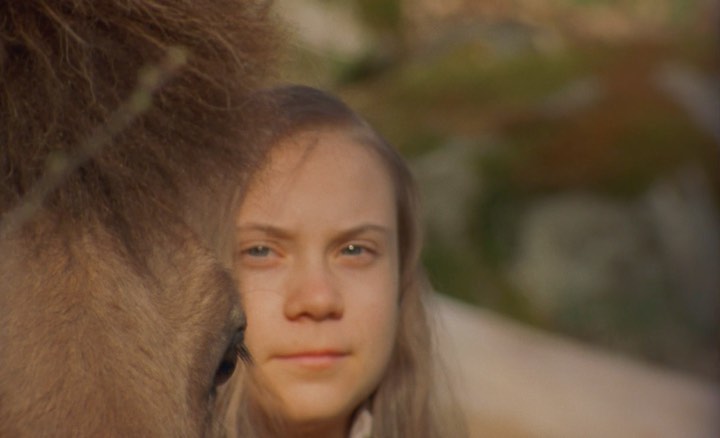 Close-up shot of a Caucasian young adult female with blonde hair, captured in an outdoor setting with greenery and fur visible.