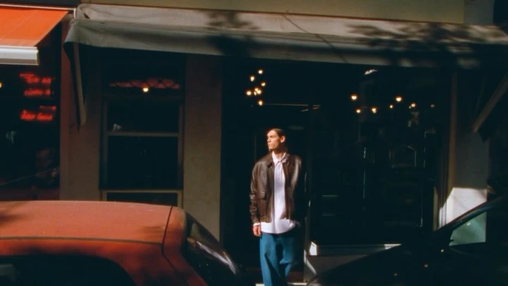 Man wearing a brown leather jacket and blue trousers walking outside a storefront in Paris directed by Emir Eralp