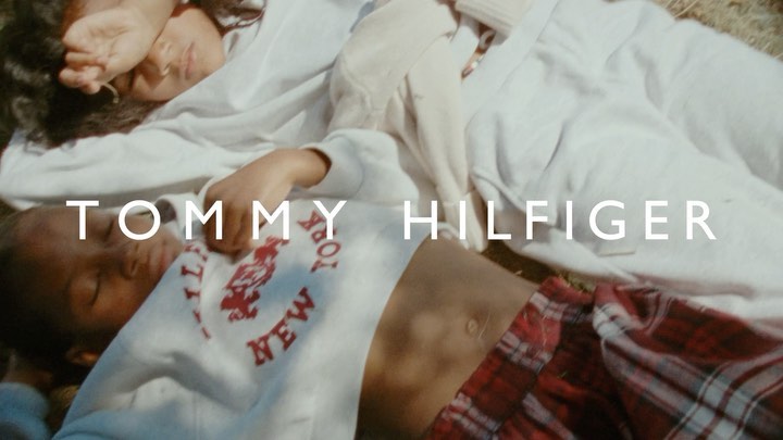 Two young adults relax outdoors in a sun-drenched campaign for Tommy Hilfiger, clad in casual sweatshirts and plaid pants.