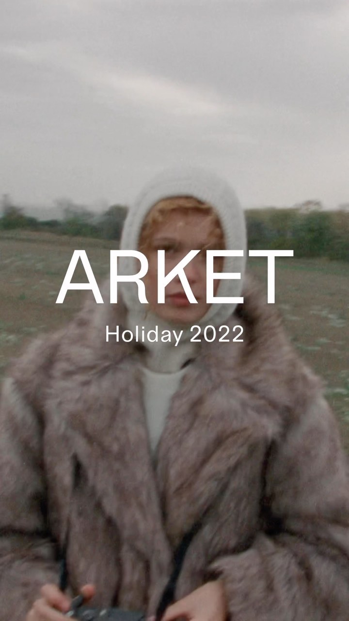 A person wearing a fur coat and hoodie stands in a field on a cloudy day. Text overlays the image including brand and holiday information.