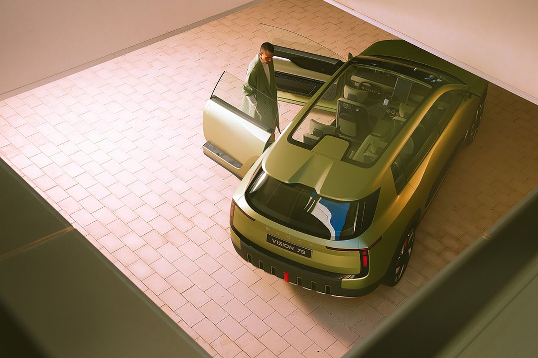 Olive-green futuristic SUV with a gull-wing door open, viewed from above inside a garage-like space, revealing the interior and modern design.