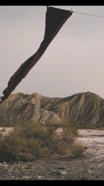Cloth hanging on a line in a desolate, arid landscape, showcasing textures of cloth and earth with a muted color palette.