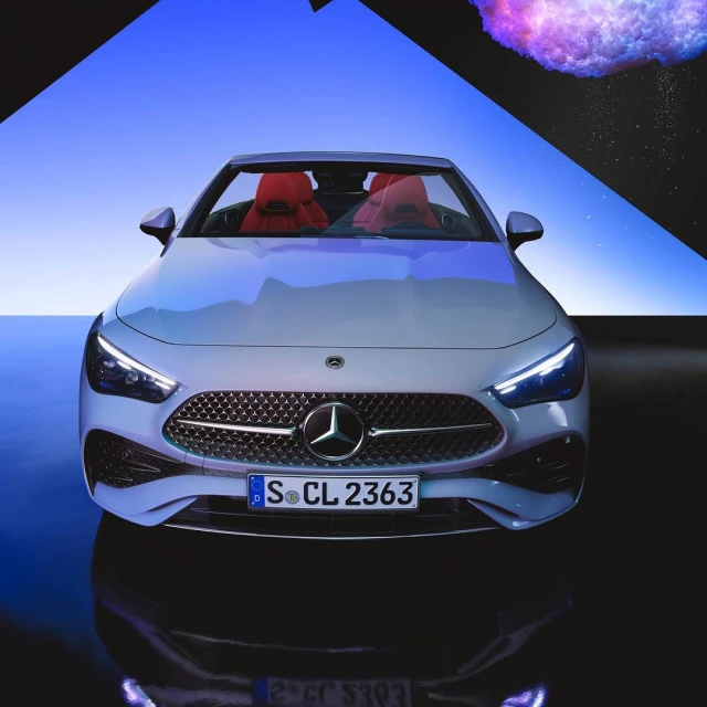 Front-angle studio shot of a white Mercedes-Benz, showcasing its grille, headlights, and sleek design, with a blue and black abstract backdrop.