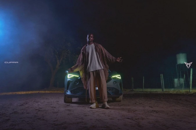 Man in casual wear poses in front of the Cupra Formentor SUV against a dark outdoor backdrop with visible brand logos and signage.