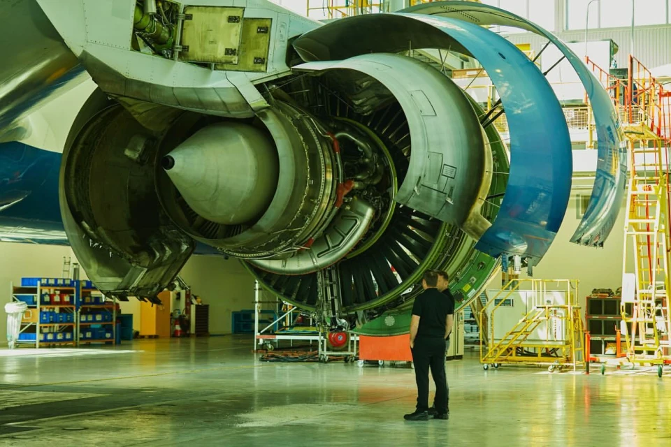 Close-up of a large jet engine undergoing maintenance in an aircraft hangar, showcasing its intricate mechanical details with workers present.