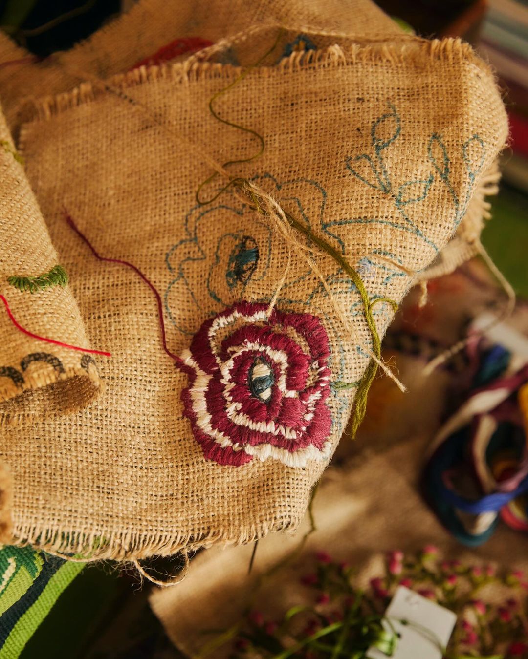 Burlap sack with floral embroidery. The embroidery is in burgundy and white, on a rough, brown burlap fabric, close-up shot.