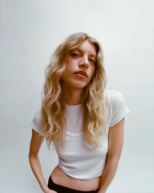 Blonde woman with wavy hair poses in a white short-sleeve shirt against a bright background in a studio portrait. Fashion shot.