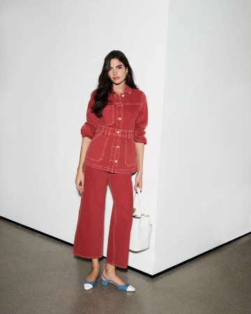 Model in red denim set holding white handbag standing against a white corner wall photographed by Emma Anderson