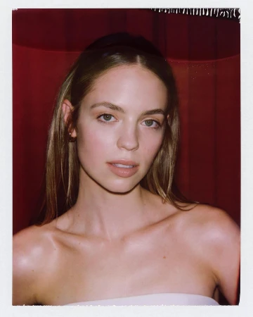 Close-up portrait of a young woman with long brown hair, light skin, and a neutral expression against a blurred red background.