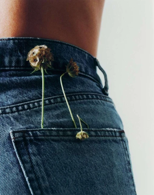 Close-up of denim jeans with dried flowers in the back pocket, showing the waist of a female. Fashion, lifestyle, and nature.