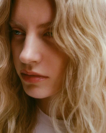 Close-up portrait of a woman with long blonde wavy hair and neutral expression photographed by Emma Anderson