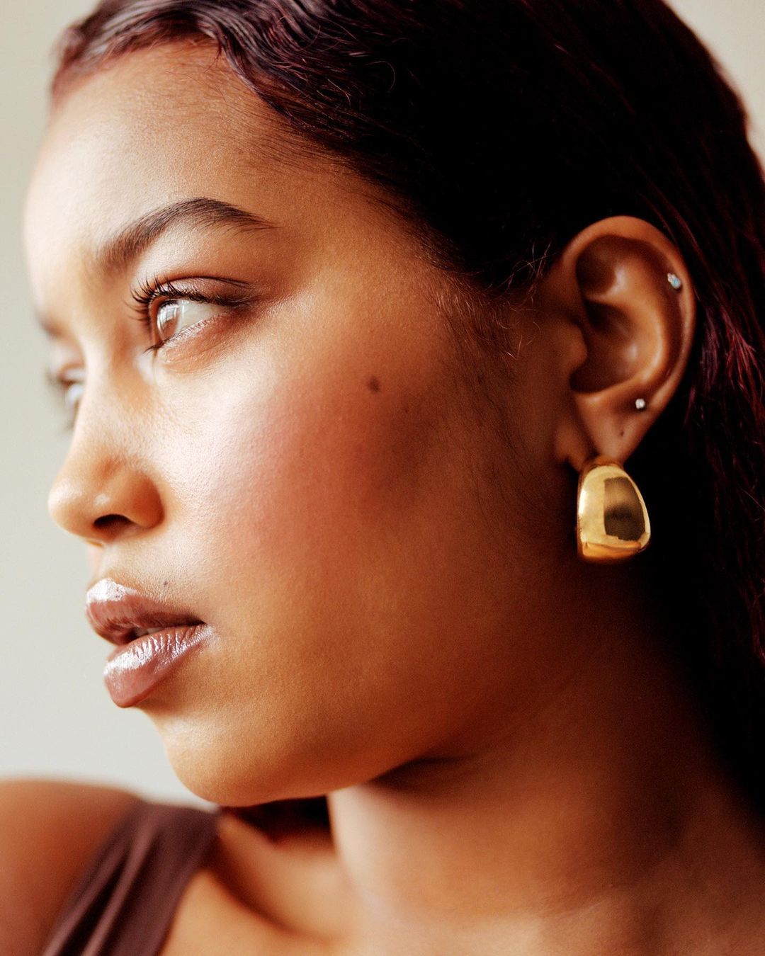 Close-up portrait of a woman with dark curly hair and golden hoop earrings, showcasing her face and profile in a beauty shot.