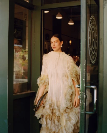 A fashionable woman in an elegant dress is walking through the green door of an establishment with white pendant lights and logo.