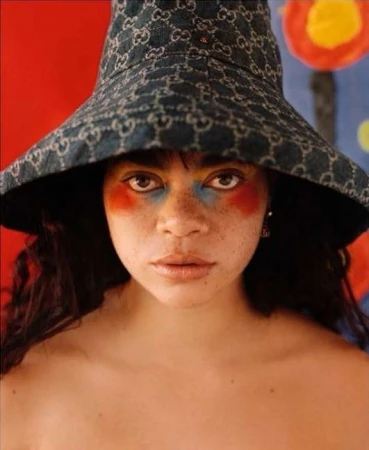 Close-up portrait of a woman wearing a monogrammed denim bucket hat and colourful face makeup by Emma Anderson