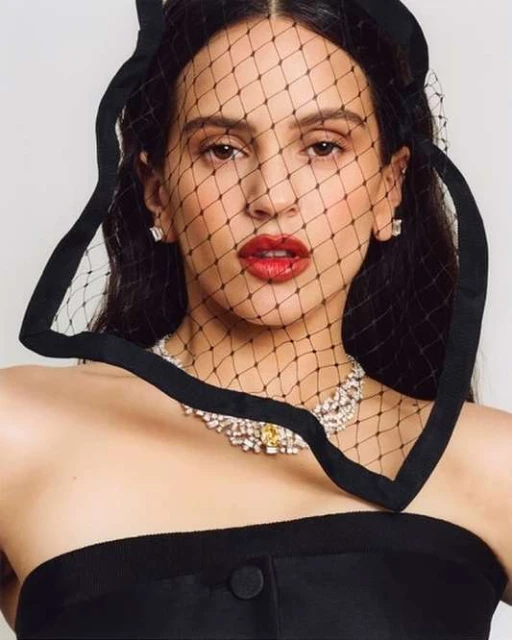 Close-up studio portrait of a young adult female with red lipstick, black net veil, and jewelry against a plain background.