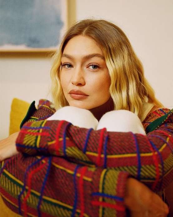 Close-up portrait of a blonde adult female wearing a plaid shirt while seated indoors with soft lighting.