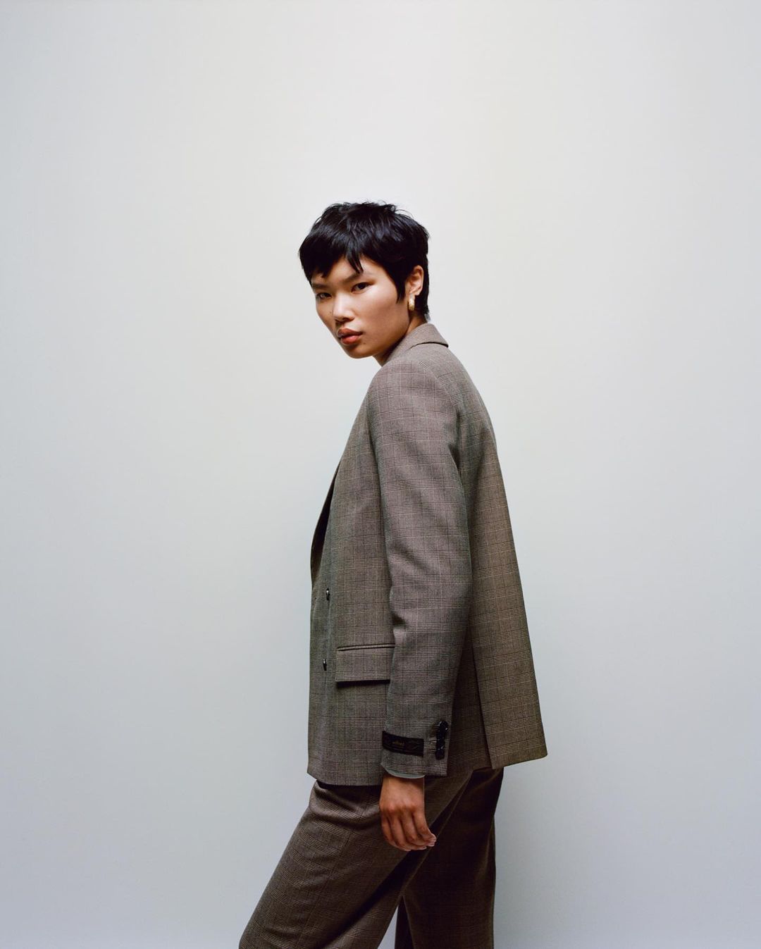 Model with short dark hair wearing a tailored brown blazer against a plain neutral background by Emma Anderson