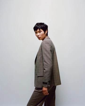 Model with short dark hair wearing a tailored brown blazer against a plain neutral background by Emma Anderson