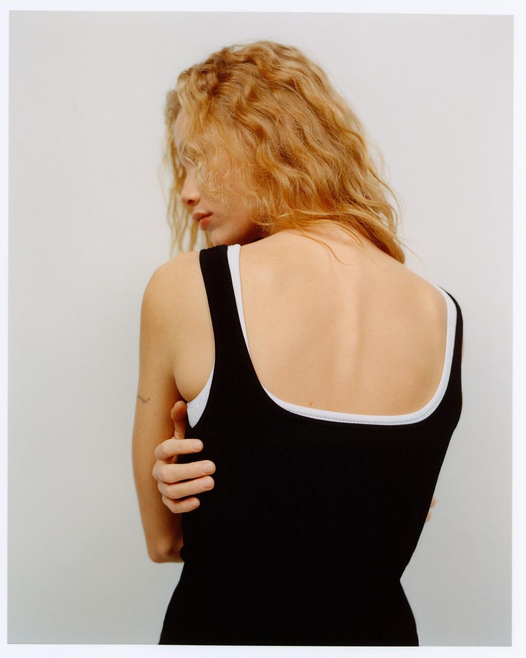Woman with long blonde wavy hair wearing a black tank top over a white top against a white background
