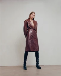Model wearing a brown leather blazer and skirt with black boots against a plain wall