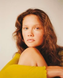 Portrait of a young woman with long brown hair wearing a chartreuse top against a plain light background by Emma Anderson.