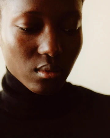 Close-up portrait of a Black woman wearing a dark turtleneck sweater against a neutral background.
