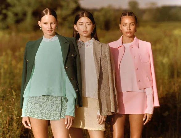 Three female models standing outdoors in a field wearing pastel and jewel-toned blazers, sweaters, and skirts by Emma Craft