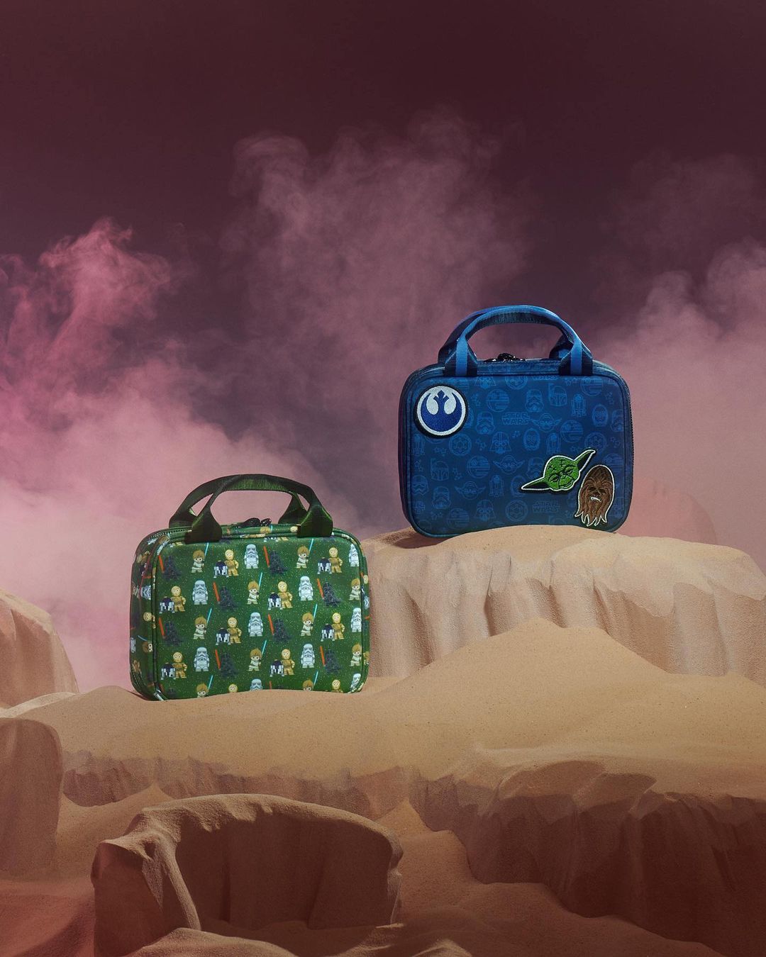 Two Star Wars themed lunchboxes featuring Yoda and Chewbacca on a sandy surface with pink smoky background, product photography.