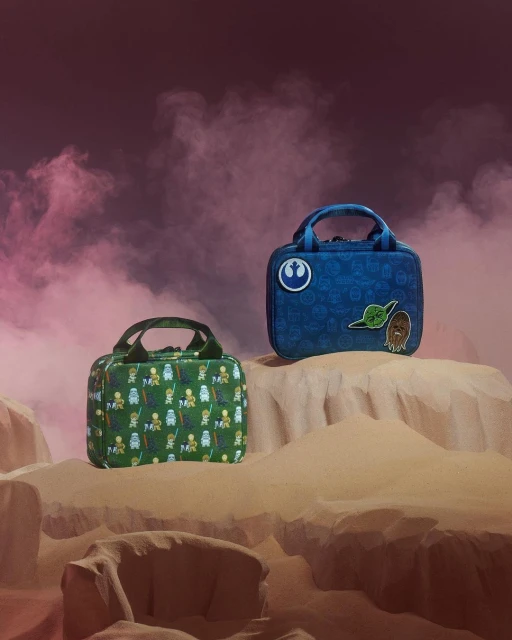 Two Star Wars themed lunchboxes featuring Yoda and Chewbacca on a sandy surface with pink smoky background, product photography.