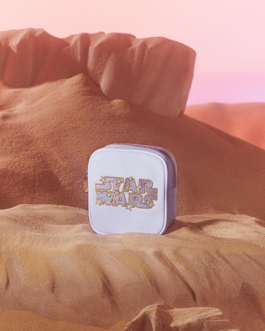 Star Wars themed bag with graphic logo on a sandy dune background, against a soft pink gradient sky, evoking a desert landscape.