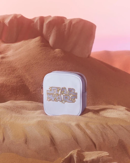 Star Wars themed bag with graphic logo on a sandy dune background, against a soft pink gradient sky, evoking a desert landscape.