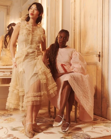 Two female models in textured dresses pose in an interior room with wooden doors and a floral rug, photographed by Emma Craft.