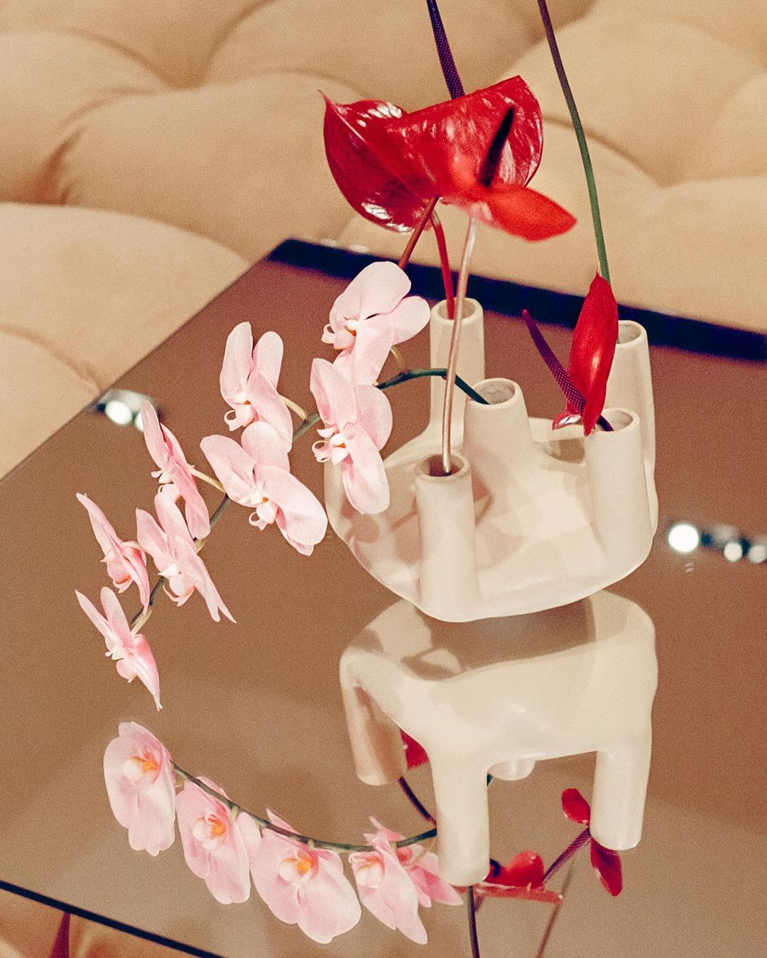 Floral arrangement featuring pink orchids and red anthuriums in a ceramic vase with a reflective tabletop surface and a soft, diffused lighting.