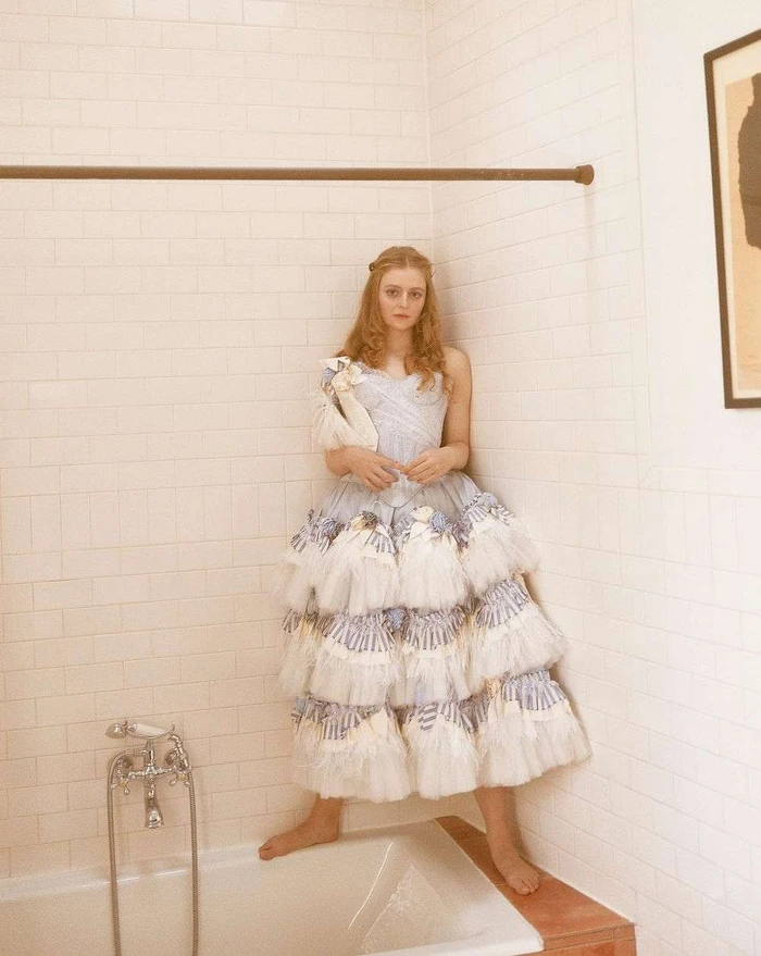 Young woman in a ruffled tiered dress standing in a bathroom next to a bathtub.