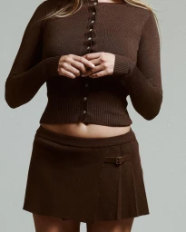 Woman wearing a brown buttoned cardigan and matching miniskirt against a plain grey textured studio background.