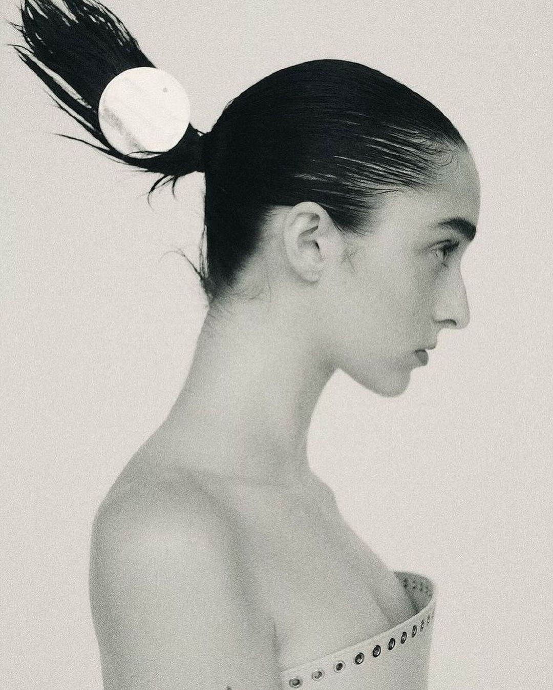 Monochromatic fashion portrait of a young adult female with dark hair styled in a ponytail, wearing a light colored top.
