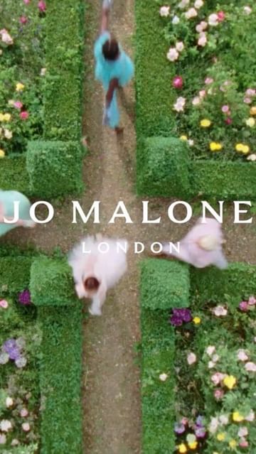 Overhead aerial view of models walking along a hedge-lined garden path with Jo Malone London text overlay in a bright, summery scene.