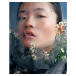 Close-up portrait of an East Asian woman draped in sheer blue tulle and woven with small white daisies.