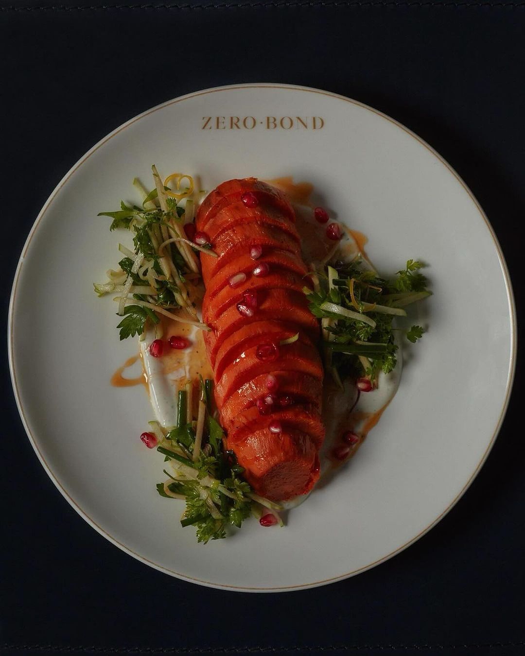 Overhead view of a sliced red-orange food item drizzled with pomegranate seeds and garnished with greens on a white plate.
