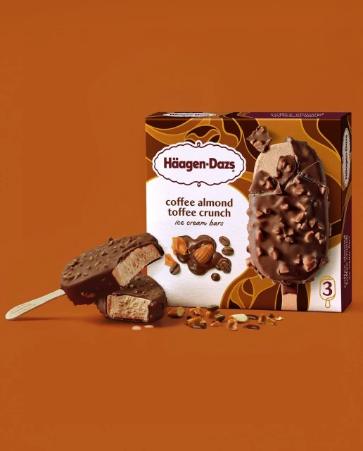 Haagen-Dazs coffee almond toffee crunch ice cream bars, one halved on a stick, with the product box in a studio setting.