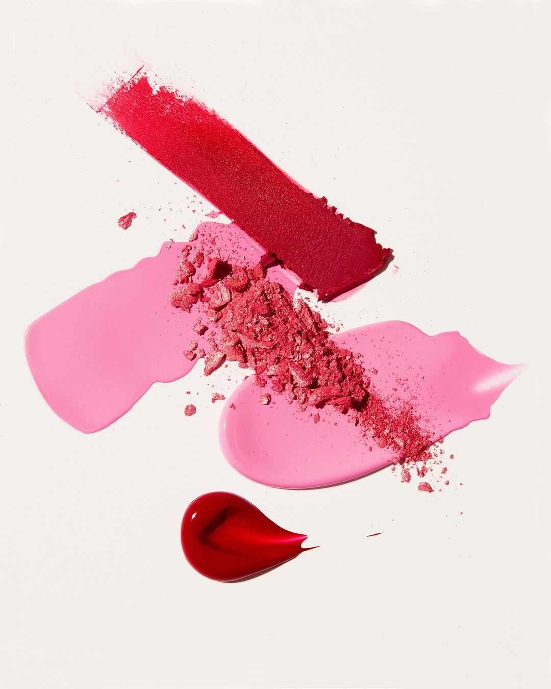 Cosmetics swatches of red and pink lipstick and blush on a white surface creating an abstract beauty product presentation.