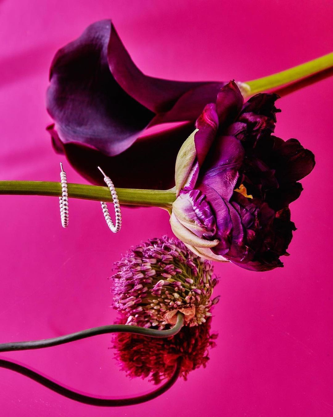 Stud earrings displayed with tulips, showcasing the jewelry on a glossy magenta surface in a product-style arrangement.