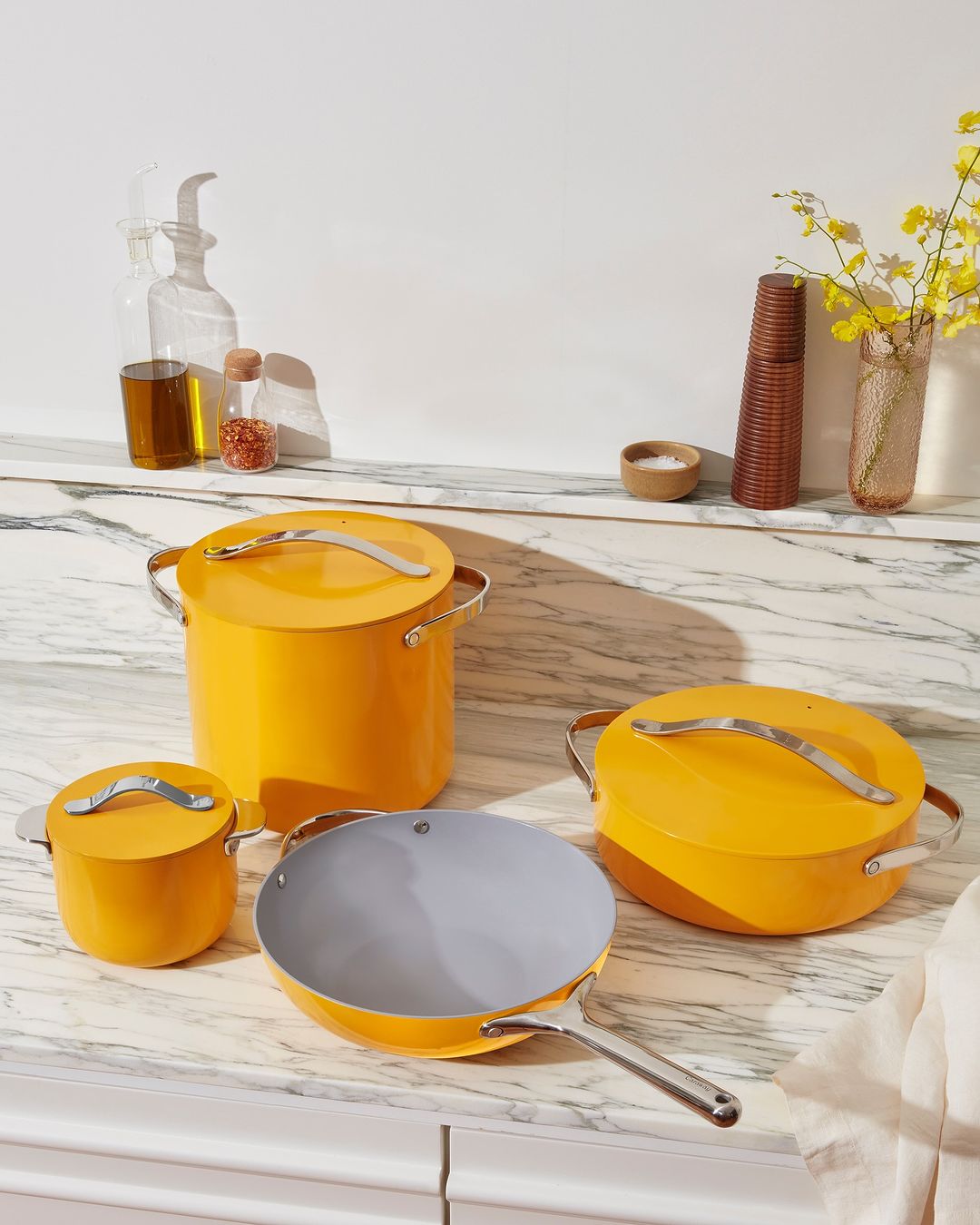 Still life of yellow cookware set including pots, pans, and lids on a marble countertop in a bright, minimalist kitchen setting.