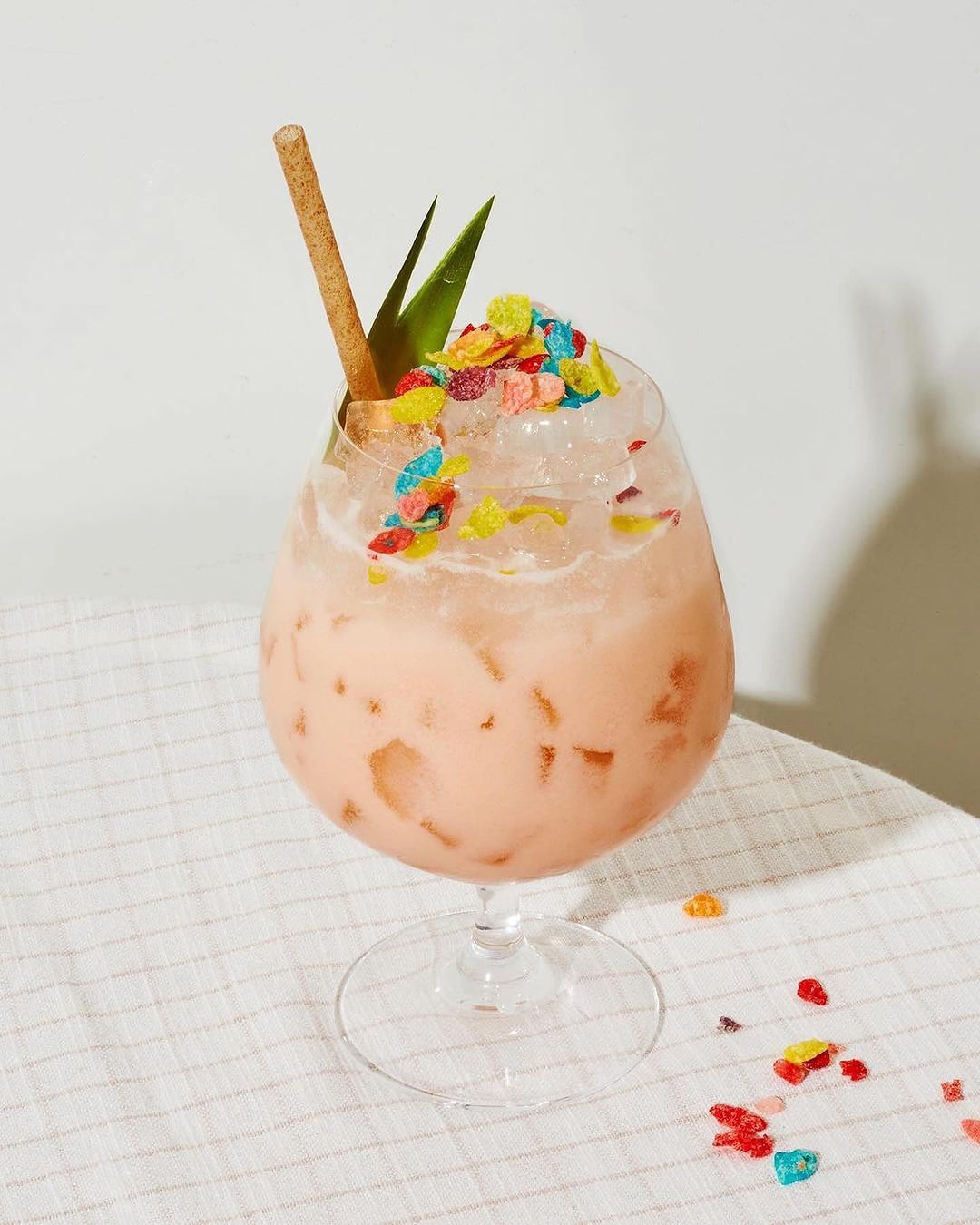 Fruity cocktail in a clear glass with a brown straw and green leaf garnish, served on a white tablecloth. Refreshing drink still life.