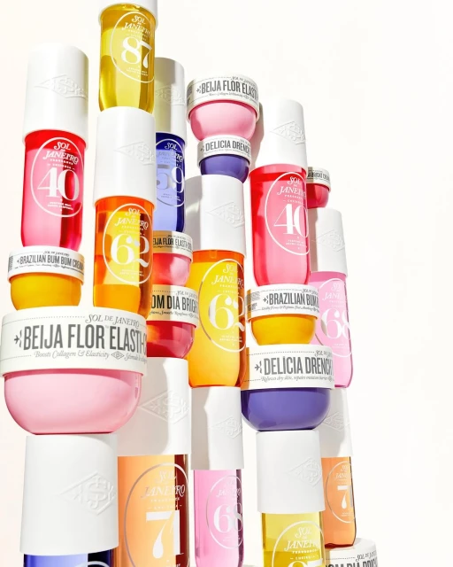 Still life studio shot of several brightly colored Sol de Janeiro body creams and lotions stacked high on a white surface.