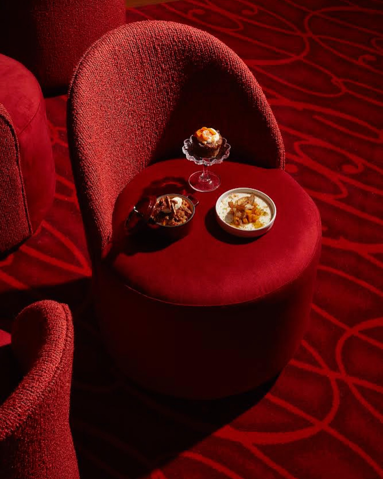 Elevated view of a cupcake, plated entrees, and a red upholstered chair with matching patterned carpet in a warm-toned interior.