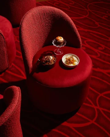 Elevated view of a cupcake, plated entrees, and a red upholstered chair with matching patterned carpet in a warm-toned interior.
