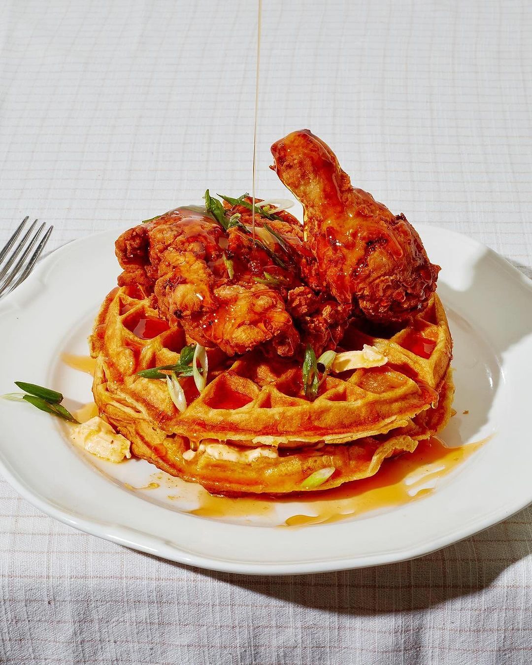 Delicious chicken and waffles drizzled with syrup on a white plate, featuring fried chicken, waffle texture, and syrup drizzle.